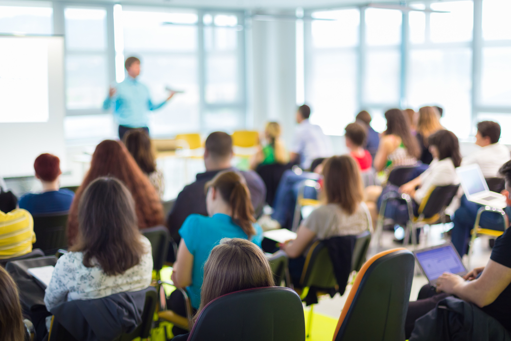 Teacher using books and AI tools in a modern classroom.